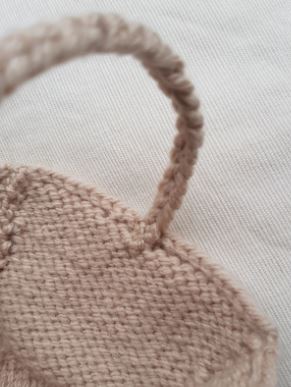 Close-up of a knitted beige hat with a handle on a light background.