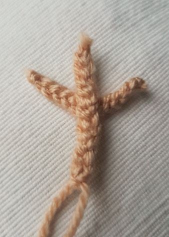 Close-up of a single light tan knitted reindeer antler, shaped with three branches and laid flat on a cream fabric background.