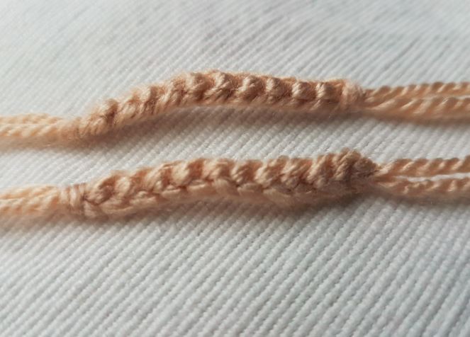 Two light brown knitted branches intended for a reindeer antler, each curved and lying flat on a textured cream fabric surface.