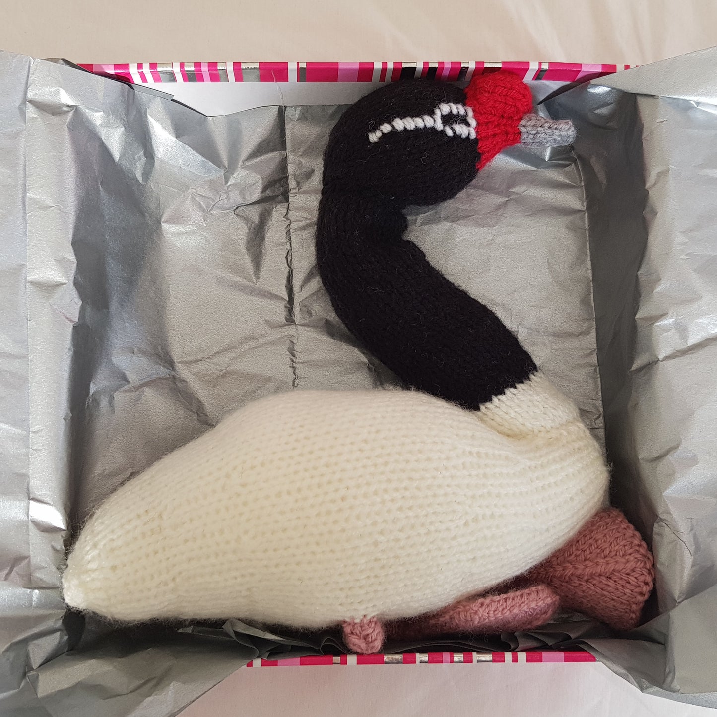 Knitted swan toy inside a box with silver interior
