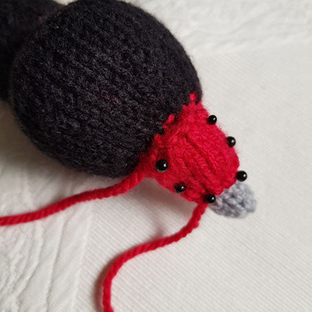 Knitted black necked swan toy close-up view of black head and red beak on a white background