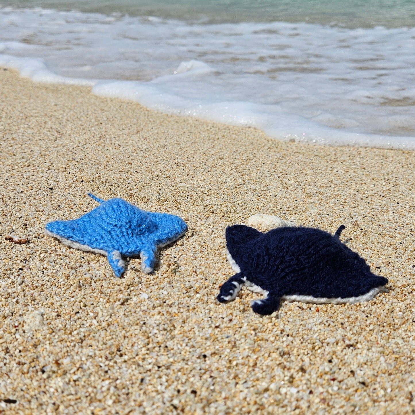 Handmade knitted manta ray toys displayed in a group on sandy beach.