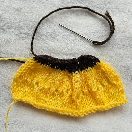 Yellow knitted fabric with black yarn and a needle on a gray background