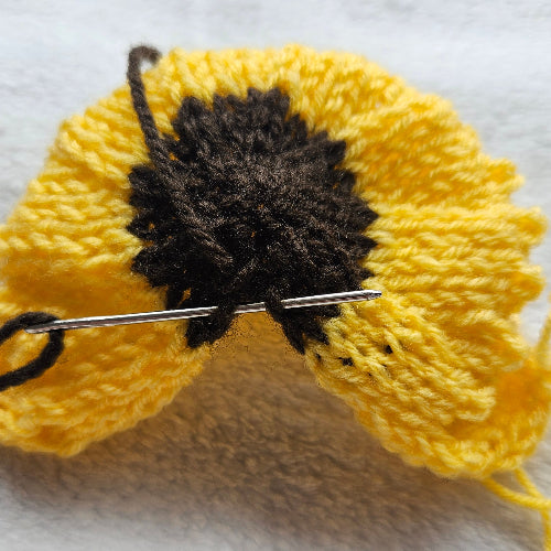 Yellow knitted flower with a black center on a white background