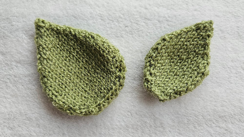 Two green knitted leaf-shaped items on a white background