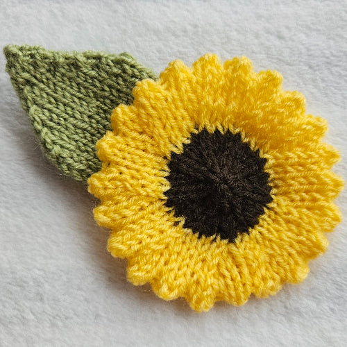 Knitted sunflower with a green leaf on a light gray background