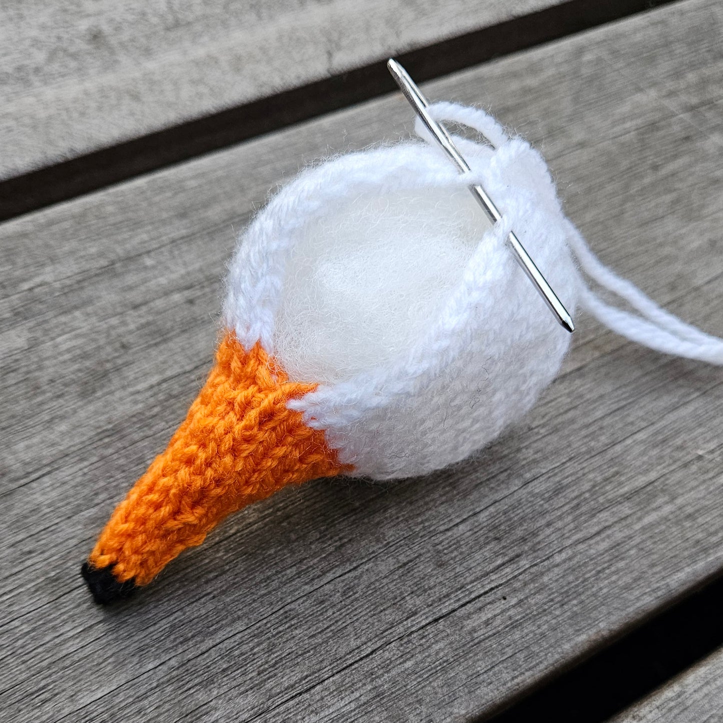 Knitted mute swan head with orange beak and white head on a wooden surface