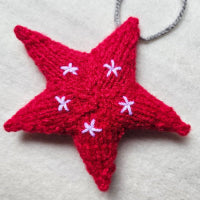 Red knitted star ornament with white flowers on a gray background