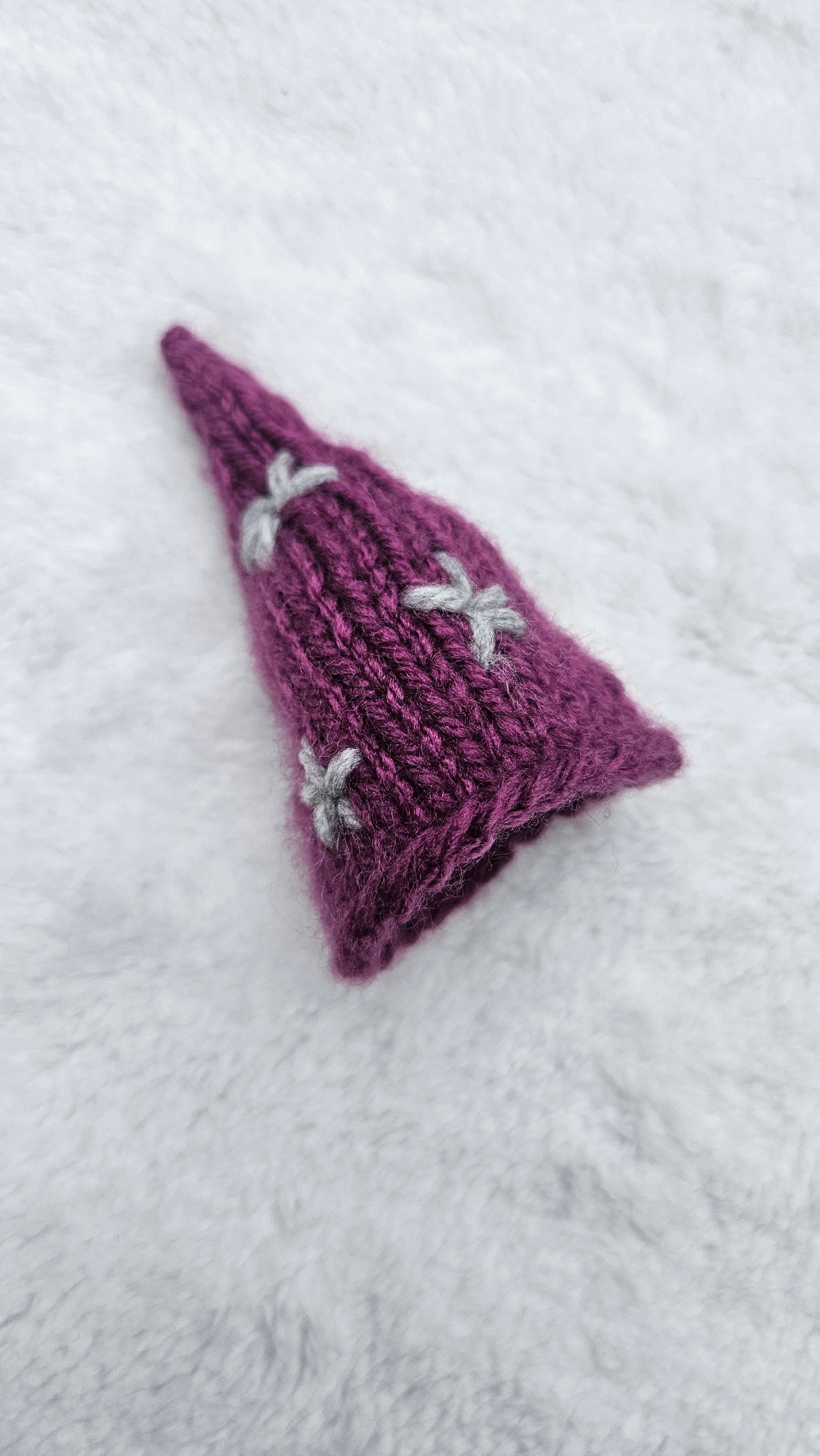 Purple knitted triangle with white patterns on a white background