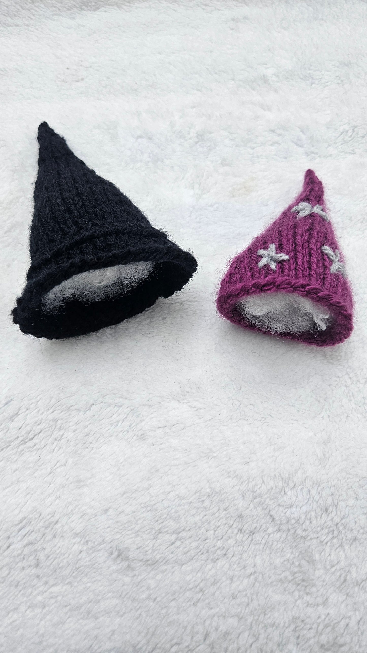 Purple and black knitted hats on a white textured surface