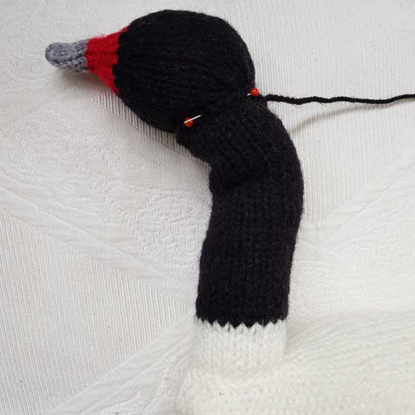 Knitted swan toy with red beak and black body on a white textured background