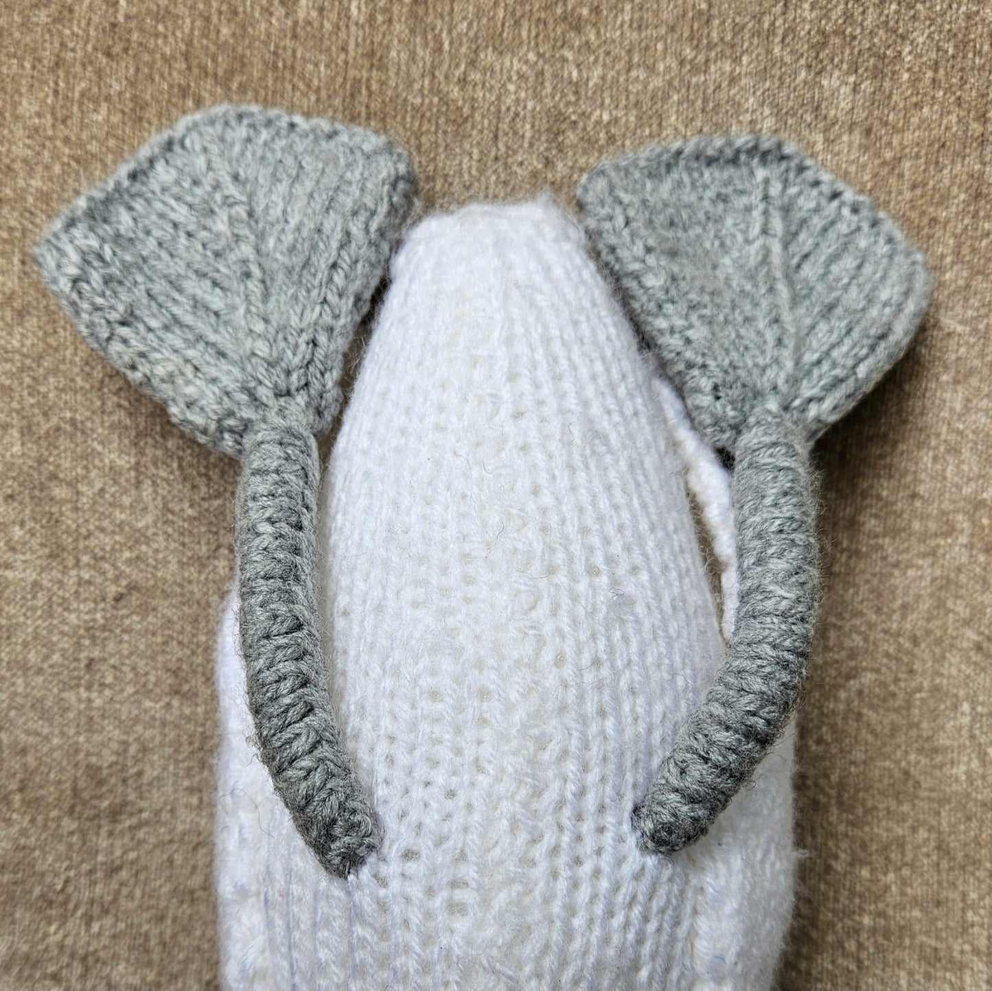 White knitted mute swan toy with gray knitted swan feet on a beige background
