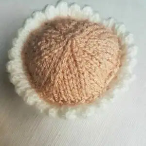 Knitted beige cupcake base with white trim on a light wooden surface