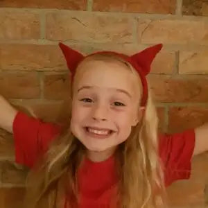 Child wearing red devil horns and a red shirt against a brick wall.