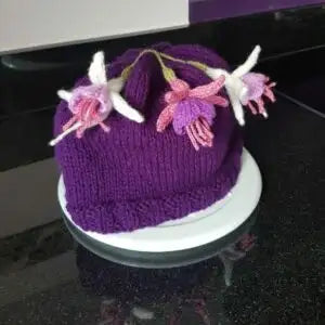 Purple knitted hat with floral decorations on a reflective surface