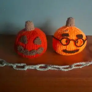 Two knitted pumpkins with faces on a wooden surface.