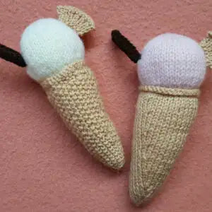 Two knitted ice cream cones with white ice cream on a pink background