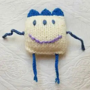 Crocheted toy with blue hair and legs on a textured white background