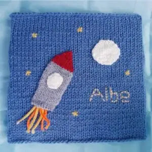 Knitted blanket with a rocket design and 'Albe' text on a blue background