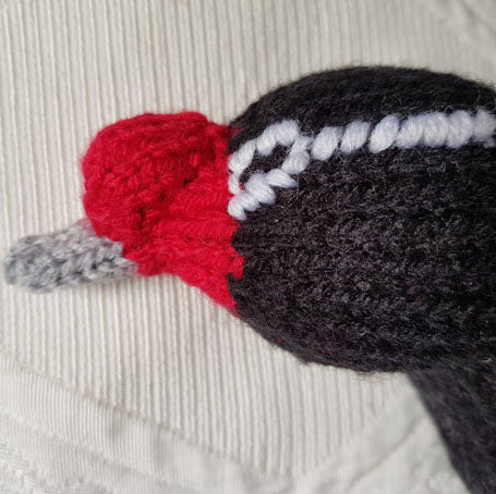 Close-up of a knitted black necked swan head with a red beak on a textured beige background