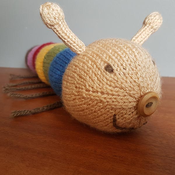 Knitted caterpillar with colourful body segments on a wooden surface.