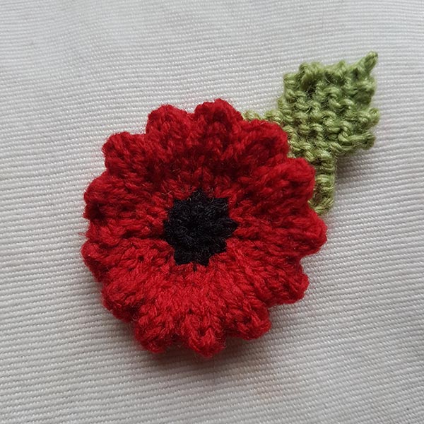 Wavy Edge Knitted Poppy with leaf, finished and ready to wear.