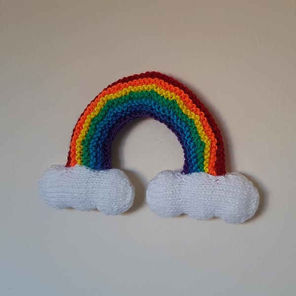 Knitted rainbow with white clouds at each end, ready for display.