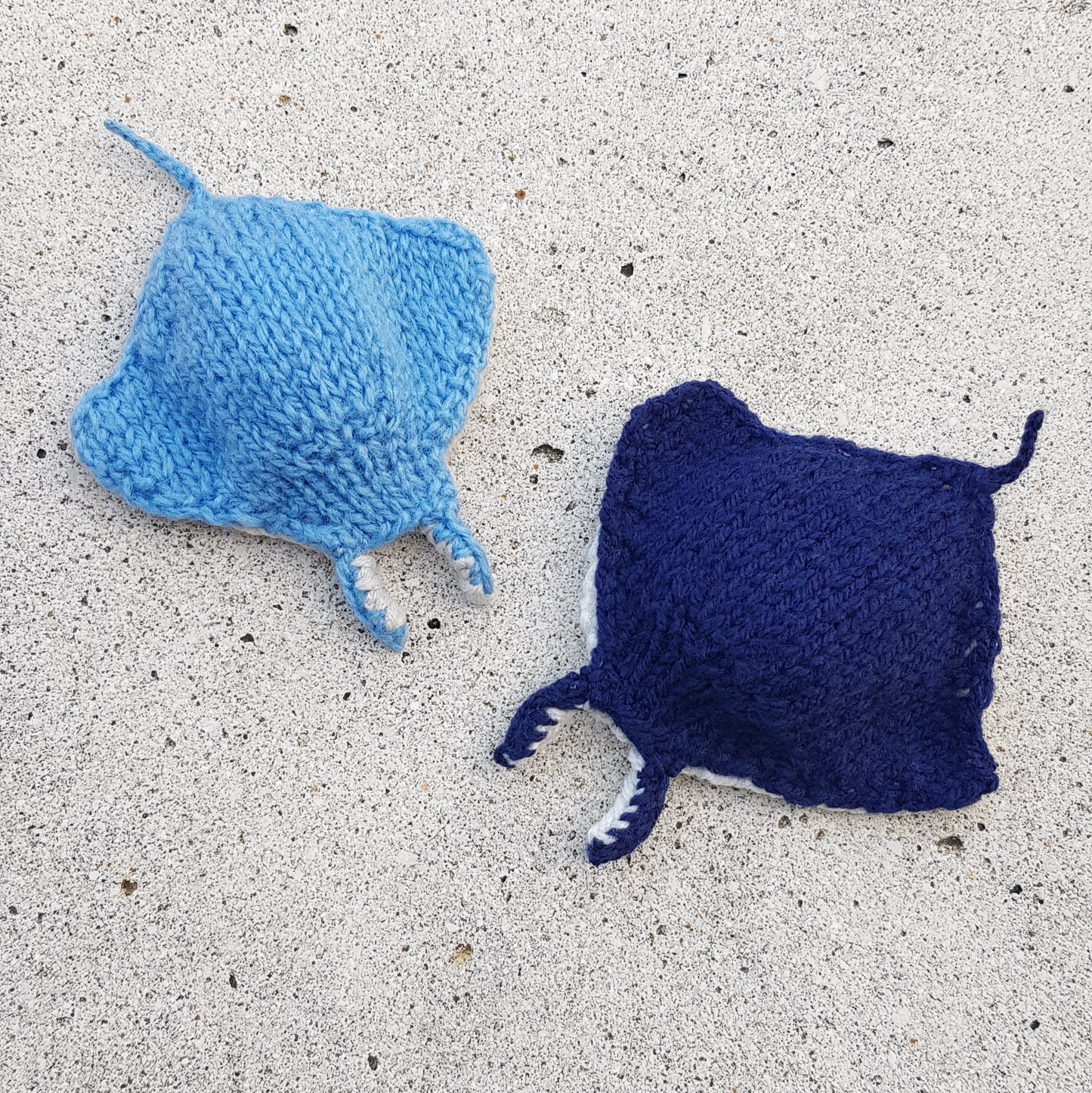 Light blue and dark blue knitted manta ray toys relaxing under the sun.