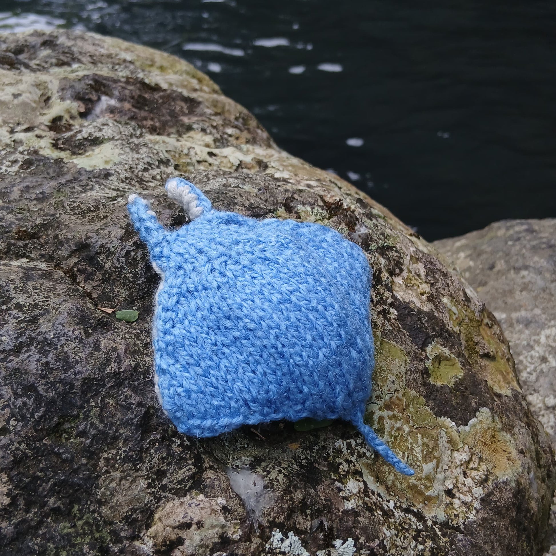 Knitted manta ray toy positioned on seaside rock, showcasing its handmade detail.