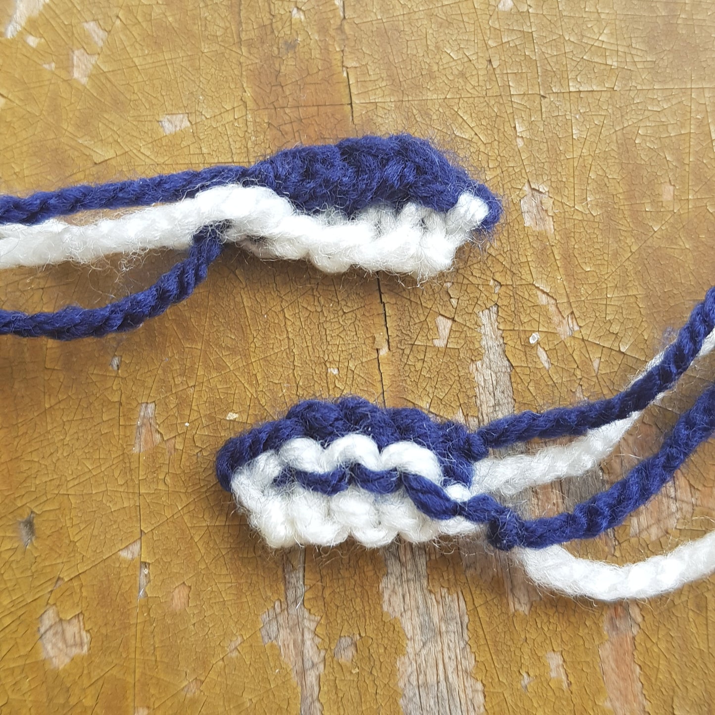 Two knitted manta ray mouthpieces in navy and white yarn, laid out on a rustic surface.