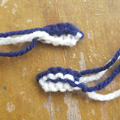 Two knitted manta ray mouthpieces in navy and white yarn, laid out on a rustic surface.