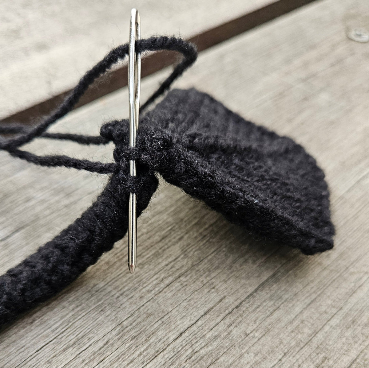 Close-up of a sewing needle joining a black knitted swan leg to its webbed foot.