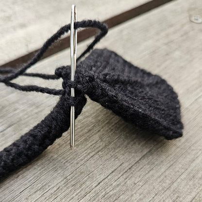Close-up of a sewing needle joining a black knitted swan leg to its webbed foot.