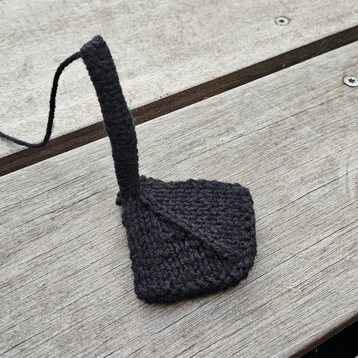 Black knitted swan leg attached to a webbed foot on a wooden surface.
