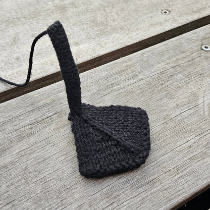 Black knitted swan leg attached to a webbed foot on a wooden surface.