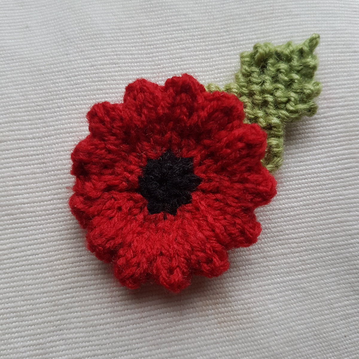 Knitted poppy flower with a green leaf on a light cream background