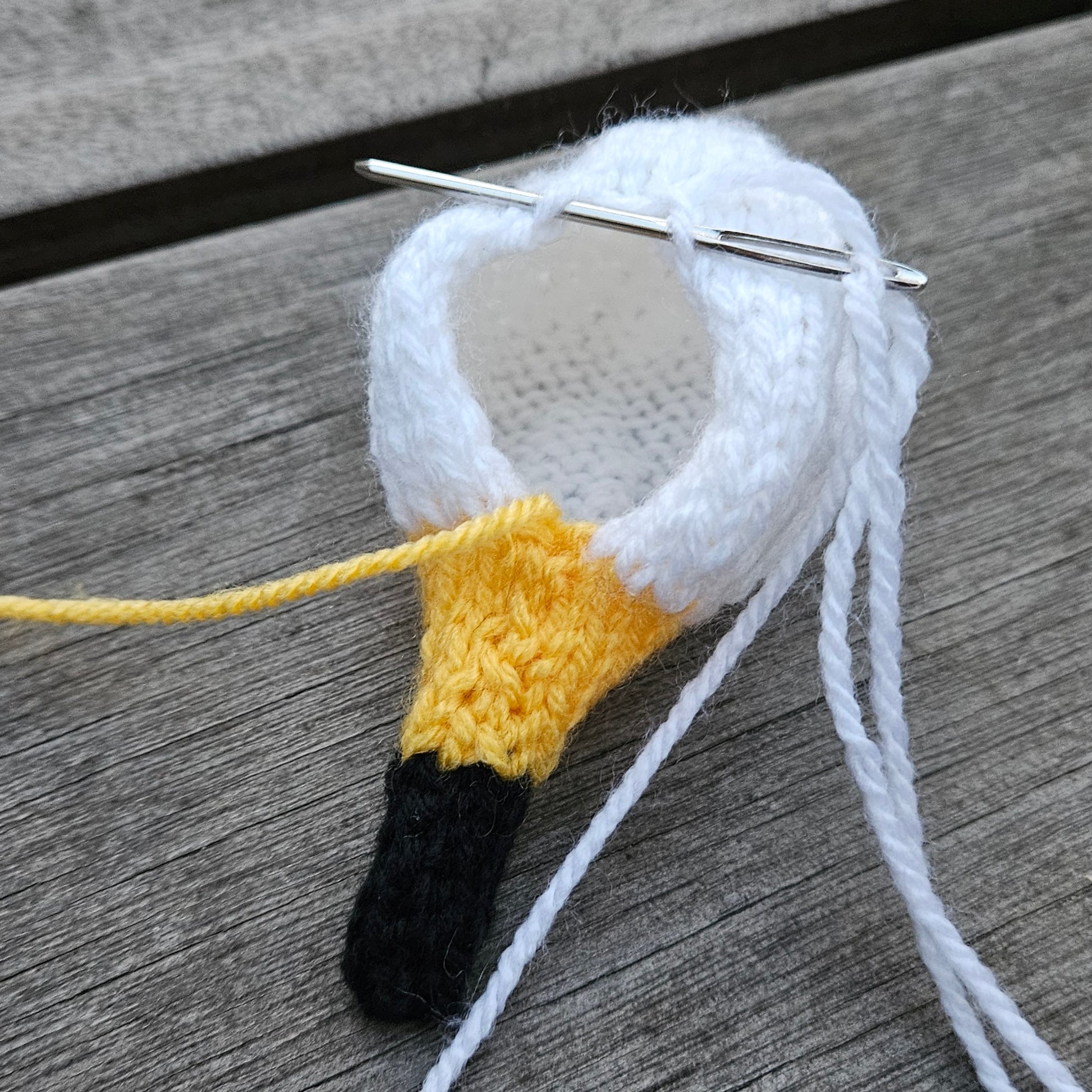 Knitted swan head with yellow beak and black bill on a wooden surface