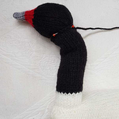 Knitted swan toy with red beak and black body on a white textured background
