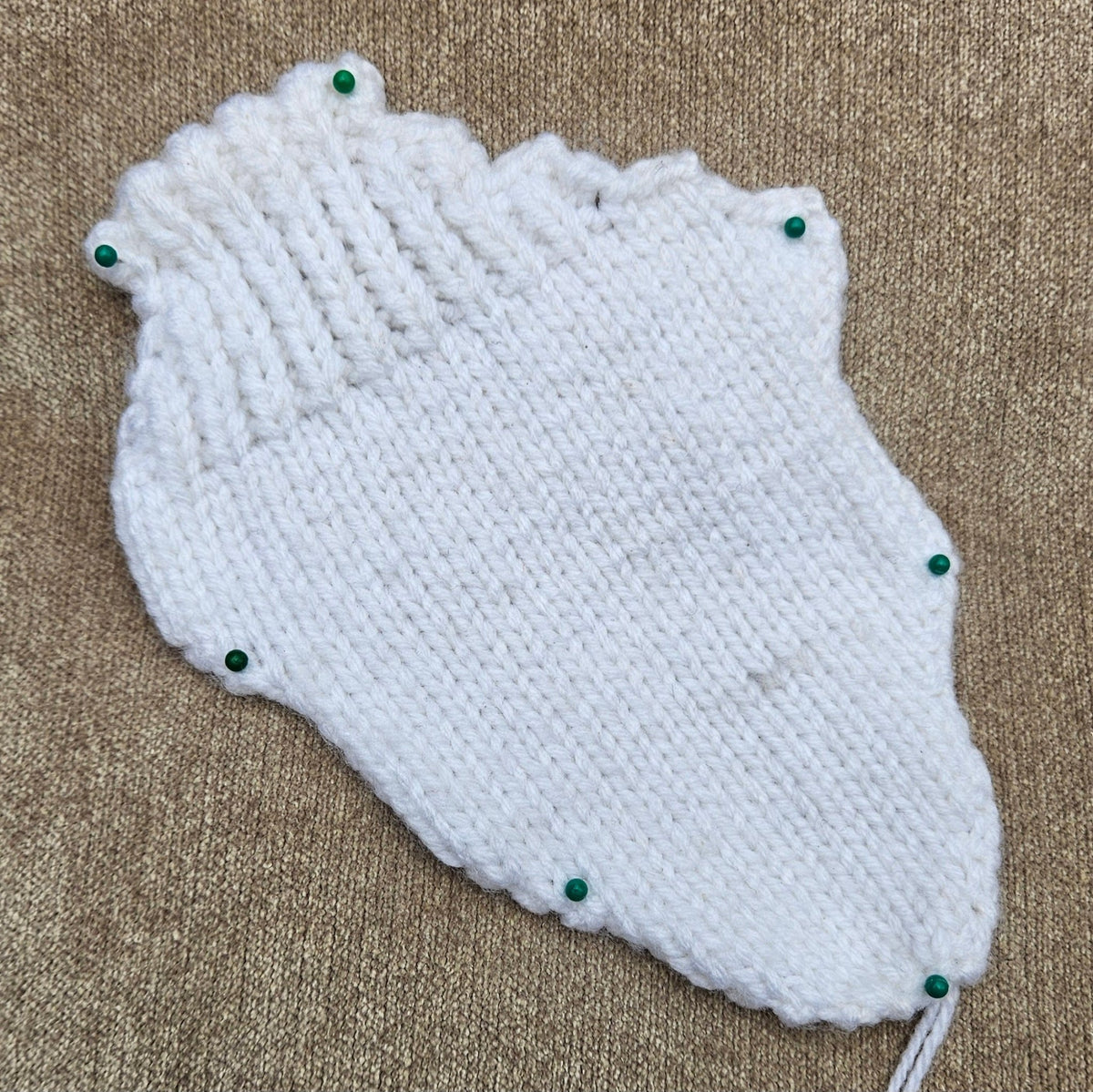 White knitted swan wing pinned flat, showing its scalloped edge and feather-like stitch detail.