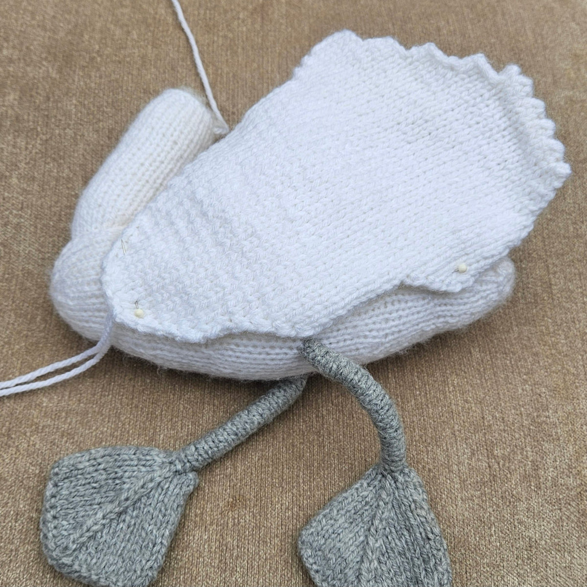 Partially assembled white knitted swan with a broad scalloped wing pinned to its body and grey legs and feet.