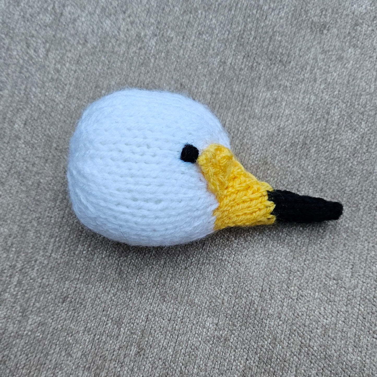 Knitted swan head resembling a golf club head on a beige surface