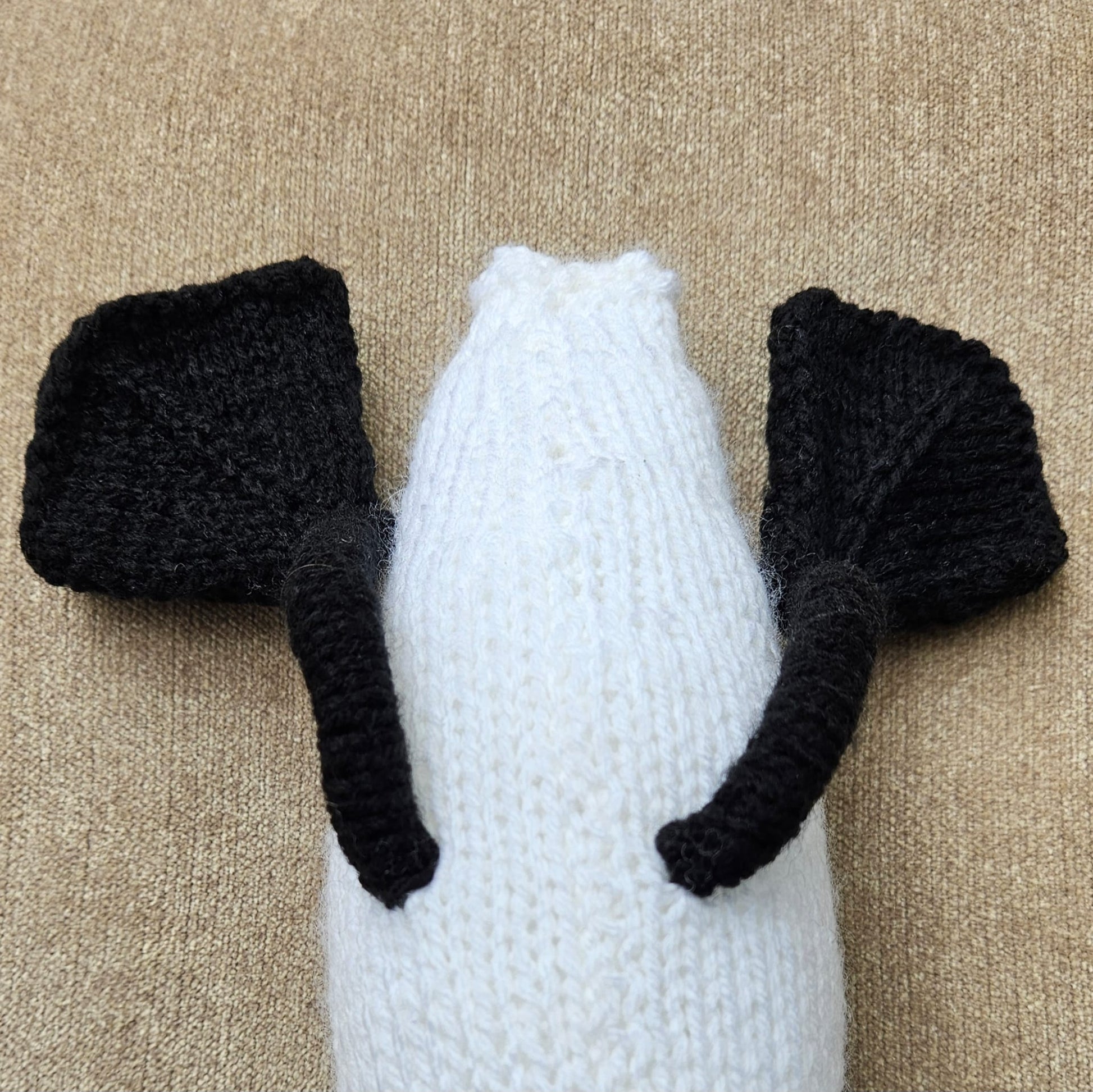 White stuffed knitted swan with black swan feet on a beige carpet