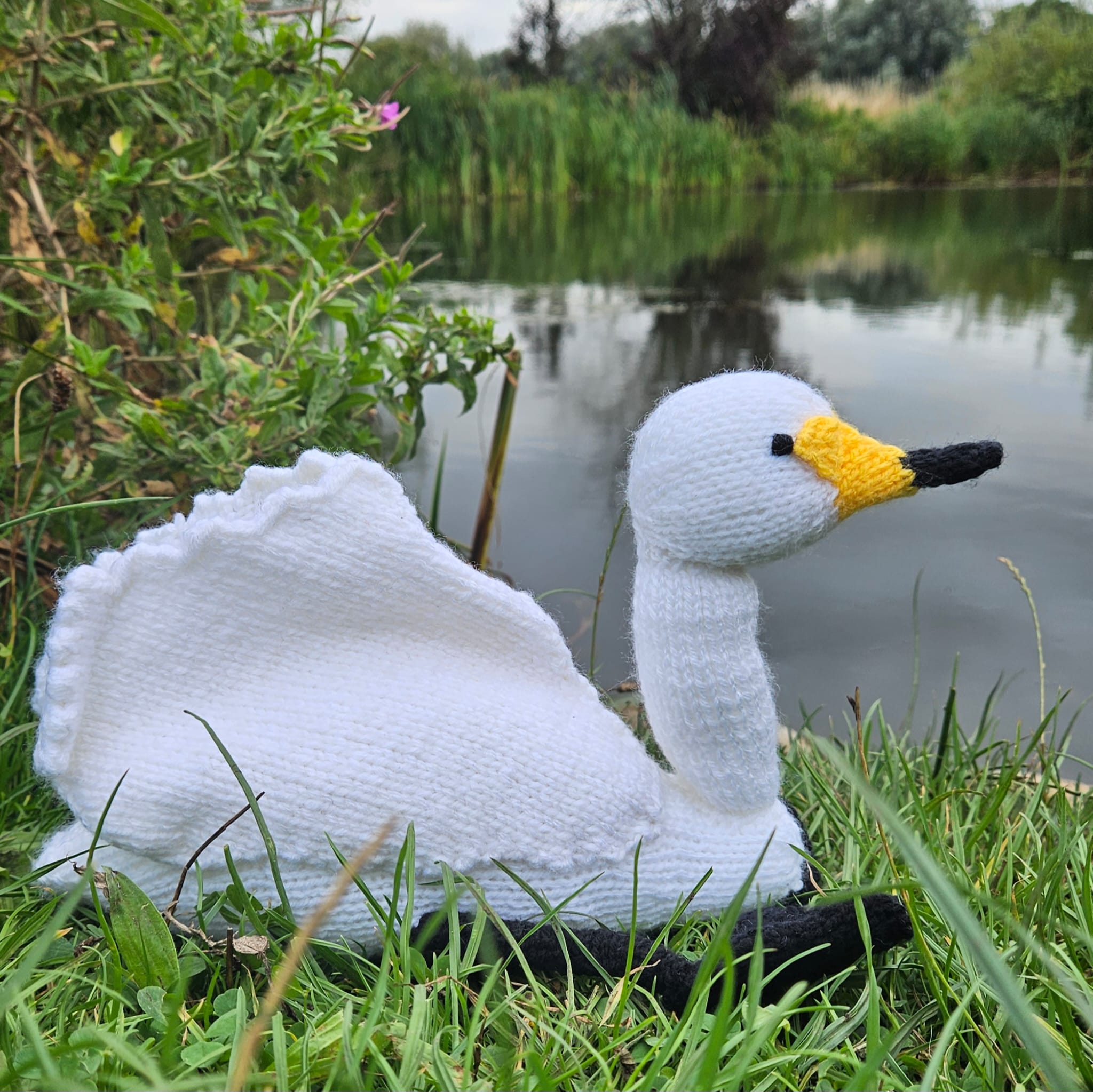 Knitted swan toy in a natural setting with water and greenery